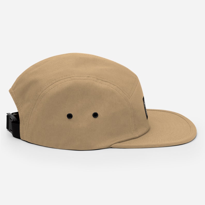 May include: A tan 5-panel cap with a black strap and a black patch on the side.