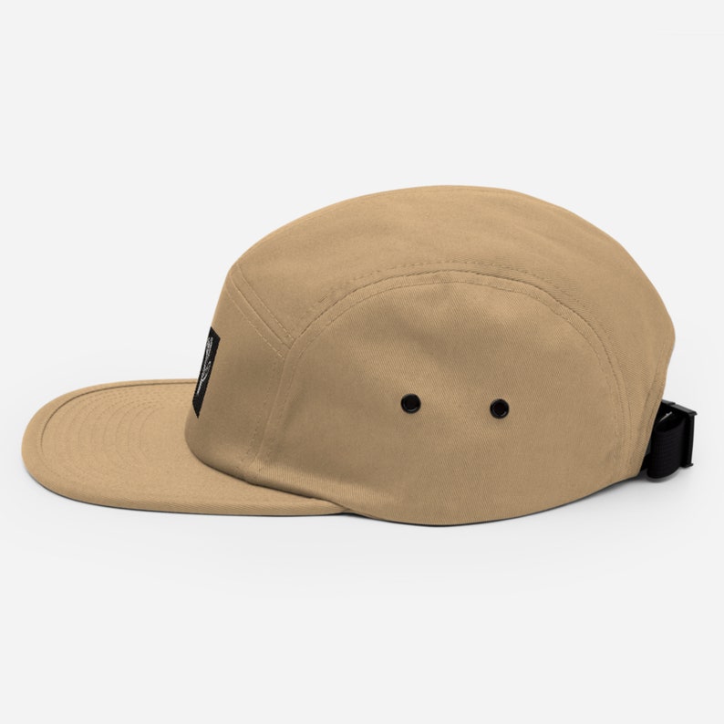 May include: A tan 5-panel cap with a black adjustable strap and a small black patch on the front.
