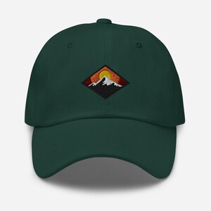 May include: A dark green baseball cap with an embroidered patch of a mountain range with a setting sun. The patch is in a diamond shape with orange, red, and yellow colors.