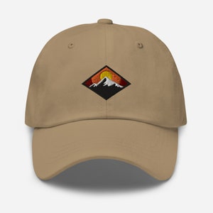 May include: A tan baseball cap with an embroidered patch of a mountain range with a setting sun. The patch is a black diamond shape with orange, red, and yellow colors.
