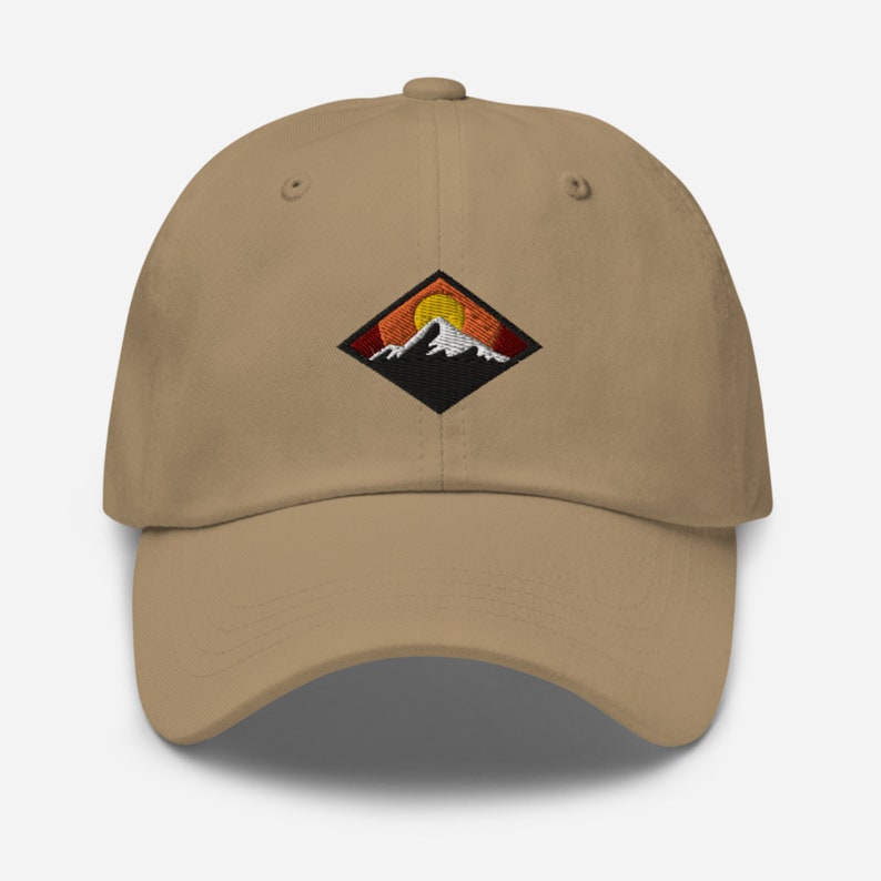 May include: A tan baseball cap with an embroidered patch of a mountain range with a setting sun. The patch is a black diamond shape with orange, red, and yellow colors.