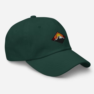 May include: A dark green baseball cap with a diamond-shaped patch featuring a mountain range and a setting sun. The patch is embroidered with orange, yellow, red, and white thread.