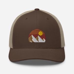 Puede incluir: Gorra de camionero marrón y beige con un diseño bordado de una puesta de sol sobre montañas. Las montañas son blancas y la puesta de sol es roja, naranja y amarilla.