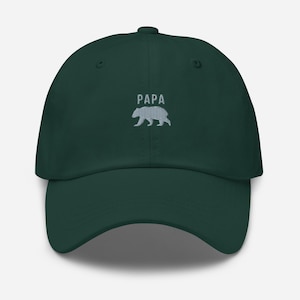 Puede incluir: Gorra de béisbol verde oscuro con la palabra "PAPA" bordada sobre una silueta de oso. La gorra tiene una visera curva y una correa ajustable. El sombrero está hecho de una tela suave y duradera.