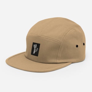 May include: A tan 5-panel cap with a black square patch featuring a white cactus illustration.