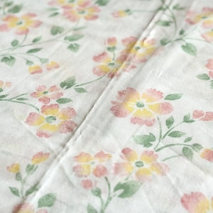 Peut inclure: Gros plan sur un tissu blanc à motifs floraux. Le motif présente des fleurs roses et jaunes avec des feuilles et des tiges vertes. Le tissu est plié, montrant la texture et le motif.