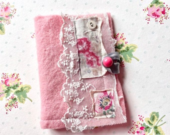 May include: A pink fabric pouch with a lace trim and a button closure. The pouch is decorated with various fabric scraps and a pink button.