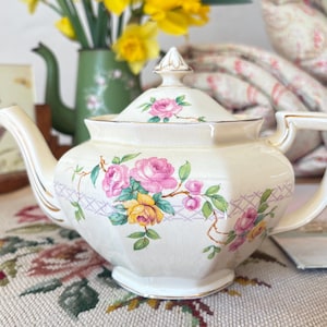 May include: A white ceramic mug with a black handle and the text "But First, Coffee" in a black, bold font. The mug is on a wooden surface. The mug is approximately 10 cm tall.