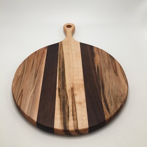 May include: Round wooden cutting board with a handle. The board features alternating vertical stripes of light and dark wood. The handle has a hole for hanging. The board is approximately 12 inches in diameter.
