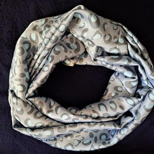 Könnte beinhalten: Ein grauer und blauer Leopardenmuster-Schal aus weichem Stoff. Der Schal ist gefaltet und zu einem Kreis gerollt.