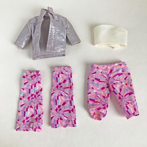 May include: A doll's outfit set comprising a silver jacket, a white top, and two skirts and a pair of trousers with a geometric pattern in pink, purple, and blue. The jacket has a shiny finish.