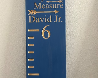May include: A blue wooden growth chart with gold lettering that reads "Loved Beyond Measure" and "David Jr." with a gold arrow pointing to the right. The chart has a gold number "6" and a series of gold lines for measuring height.