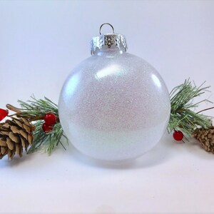 K&ouml;nnte beinhalten: Ein wei&szlig;er, schimmernder Weihnachtsbaumschmuck mit silberner Spitze.