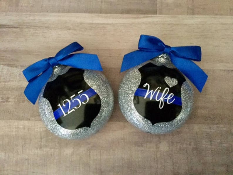 K&ouml;nnte beinhalten: Zwei silberne Glitzer-Weihnachtskugeln mit einem schwarzen und blauen Polizeibadge-Design. Eine Kugel sagt "Wife" und die andere sagt "1255".