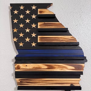 May include: Wooden American flag in the shape of the state of Georgia with a blue line representing law enforcement. The flag is made of reclaimed wood and has a distressed finish.