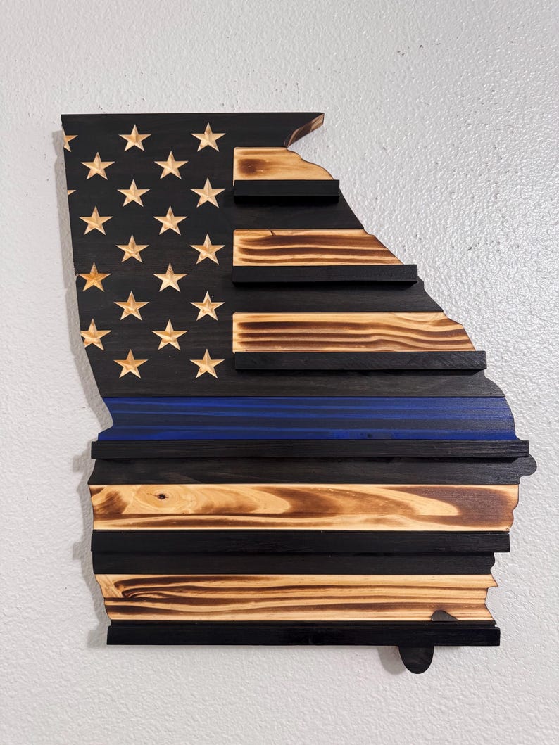 May include: Wooden American flag in the shape of the state of Georgia with a blue line representing law enforcement. The flag is made of reclaimed wood and has a distressed finish.