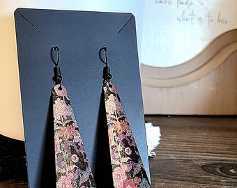 May include: A pair of long, dangle earrings with a floral pattern. The earrings are made of leather and have a black metal hook.