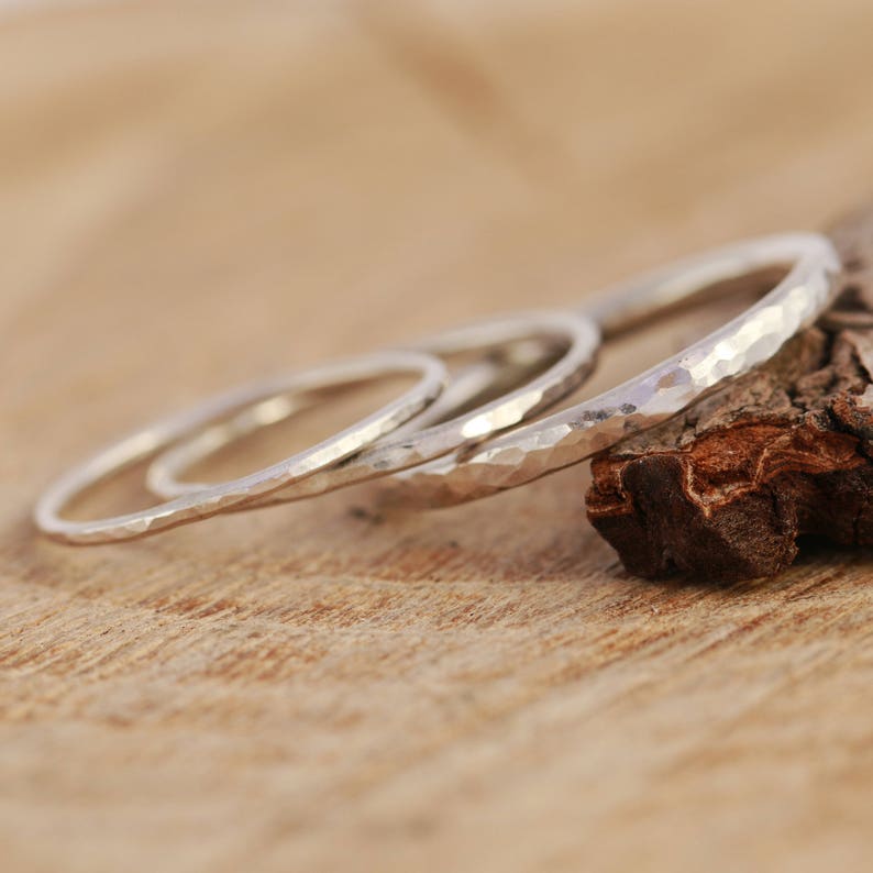 May include: Three silver hammered stacking rings on a wooden surface.