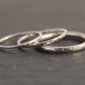 May include: Three silver hammered stacking rings. The rings are thin and delicate, with a textured surface.