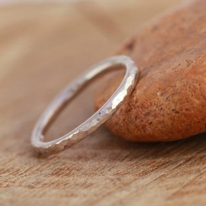 May include: A silver hammered ring with a smooth, rounded surface. The ring is sitting on a brown rock.