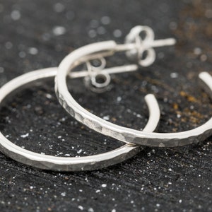 May include: A pair of silver hoop earrings with a hammered texture. The earrings are simple and elegant, and would make a great gift for any occasion.