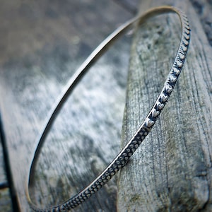 Può includere: Un braccialetto rigido in argento con una superficie testurizzata e una fila di accenti a forma di cuore.