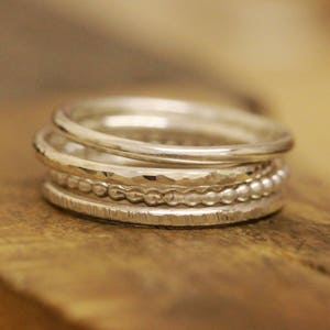 May include: A set of five silver stacking rings. The rings are all different widths and have various textures, including hammered, beaded, and smooth.
