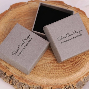 May include: Two gray boxes with the text "Silver Cave Designs Everyday is Extraordinary" printed on them. The boxes are sitting on a wooden surface.