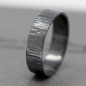以下が含まれることがあります： テクスチャ加工が施された溝のある黒い金属製のリング。リングは幅広で、磨かれた仕上げになっています。