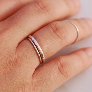 May include: Two thin silver rings with a hammered texture, worn on a finger.