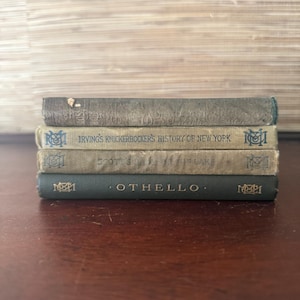 May include: A stack of four antique books with aged covers. The titles include "Irving's Knickerbocker's History of New York", "Scott's The Lake", and "Othello". The books are in shades of green, tan, and gray, with faded text and decorative emblems.
