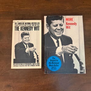 May include: Two paperback books featuring John F. Kennedy on the covers. The left book is titled The Kennedy Wit, and the right book is titled More Kennedy Wit. Both covers show a black and white photograph of Kennedy at a microphone.