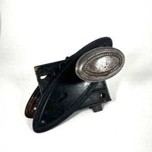 May include: Antique black door handle with an oval-shaped silver knob. The handle has a decorative pattern of small dots around the edge.