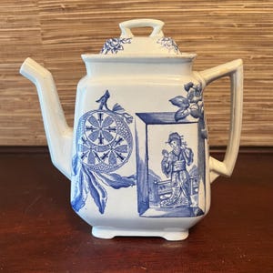 May include: A white teapot with a blue and white floral design. The teapot has a square body and a lid with a knob. The design features a woman in a kimono holding a mirror.