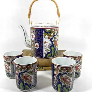 May include: A set of five porcelain teacups and a teapot with a bamboo handle. The cups and teapot are decorated with a floral pattern in shades of blue, red, gold, and green.