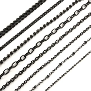 May include: Six different black metal chains of varying lengths and styles. The chains are arranged in a row from thickest to thinnest.