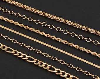 May include: A collection of five gold-toned metal chains arranged diagonally. The set includes a thick wheat chain, a round link chain, a twisted rope chain, a flat herringbone chain, and a classic oval link chain with a polished finish.
