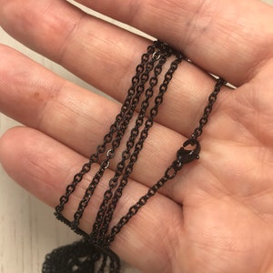 May include: A black chain necklace with a lobster clasp. The chain is made of metal and has a matte finish.