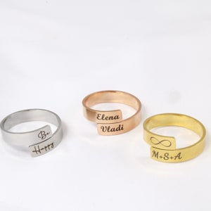 May include: Three personalised rings with engraved text. The ring on the left is silver and says "Be Happy". The ring in the middle is rose gold and says "Elena Vladi". The ring on the right is gold and says "M+S+A" with an infinity symbol.