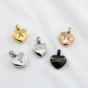 May include: Five heart-shaped pendants in gold, silver, and black. Each pendant has a loop for a chain. The gold pendant has the letter "A", the silver pendant has "KIRA", and the black pendant has a date. The rose gold pendant has "TK", and the silver pendant has "P".