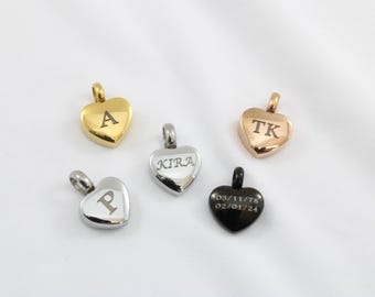 May include: Five heart-shaped pendants in gold, silver, and black. Each pendant has a loop for a chain. The gold pendant has the letter "A", the silver pendant has "KIRA", and the black pendant has a date. The rose gold pendant has "TK", and the silver pendant has "P".
