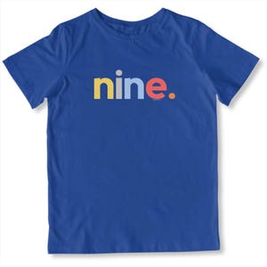 May include: A royal blue t-shirt with the word "nine." in colorful letters. The word "nine" is in yellow, blue, and red. A simple, casual design for everyday wear.