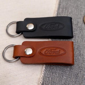 May include: Two leather keyrings with metal rings. One is brown with the word "Ford" embossed in the leather. The other is black with the word "Ford" embossed in the leather.