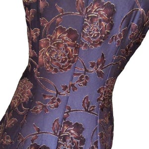 Könnte beinhalten: Nahaufnahme eines dunkelblauen Stoffes mit floralem Muster. Das Design zeigt große, samtige braune Rosen und Blätter mit goldenen Akzenten. Der Stoff scheint ein Kleid oder ein Kleidungsstück zu sein.