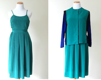 May include: Two teal blue dresses on mannequins. The dress on the left is a sleeveless, A-line dress. The dress on the right is a long-sleeved dress with a teal blue top and a black and blue patterned jacket.