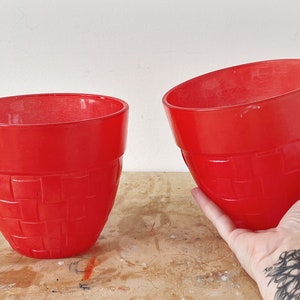 Peut inclure: Deux pots de fleurs en céramique rouge avec un motif tissé. Le plus grand pot est tenu dans une main.