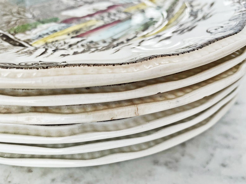May include: A stack of white ceramic plates with a brown rim and a floral design. The plates are stacked on top of each other, with the top plate showing the most detail of the design.