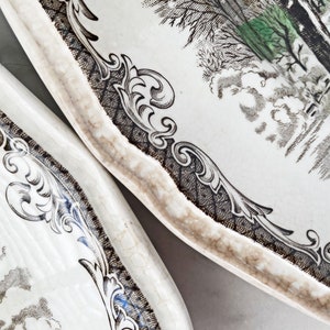 May include: Two white ceramic plates with a black and white floral design. The plates have a scalloped edge and a raised rim.