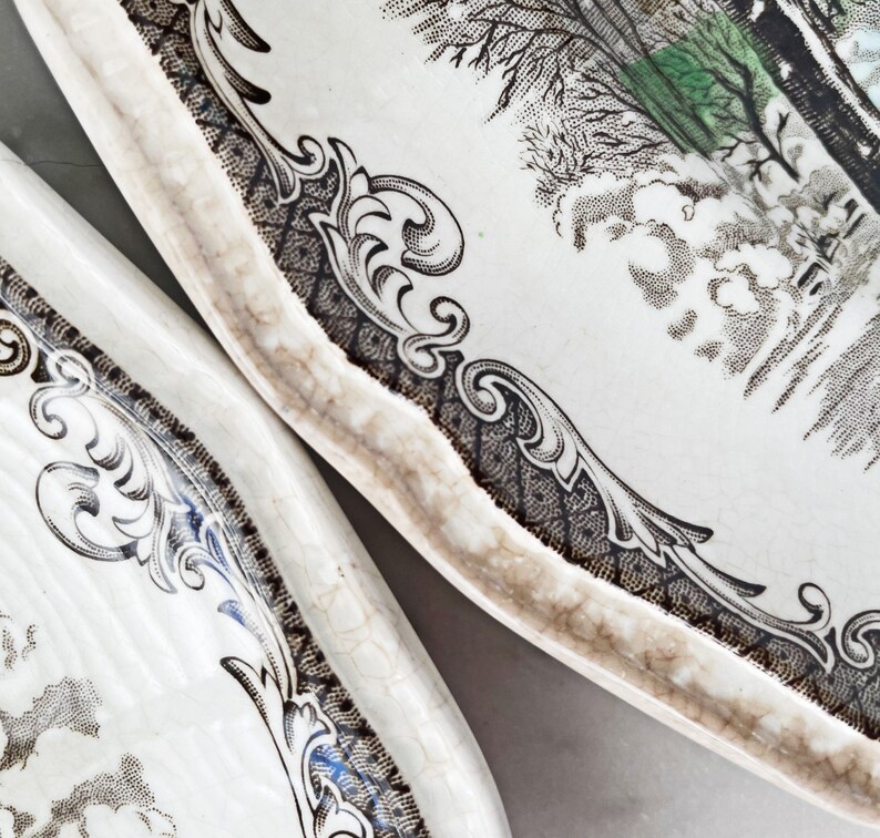 May include: Two white ceramic plates with a black and white floral design. The plates have a scalloped edge and a raised rim.