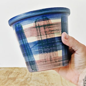 Pode incluir: Um vaso de cerâmica azul e rosa com um padrão xadrez. O vaso é pintado à mão com um efeito de pinceladas.